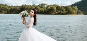 woman holding bouquet of flowers wearing wedding dress standing on dock during day