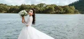 woman holding bouquet of flowers wearing wedding dress standing on dock during day