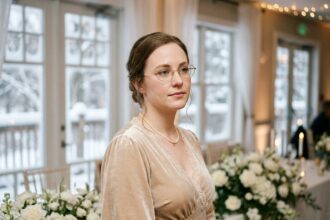 Invitée élégante portant des lunettes à monture dorée ovale lors d'un mariage d'hiver dans une salle décorée de fleurs blanches